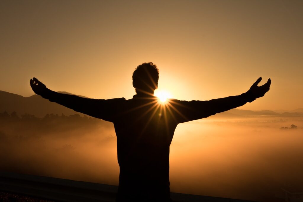 Person standing with arms open wide at sunrise, symbolizing freedom from anxiety