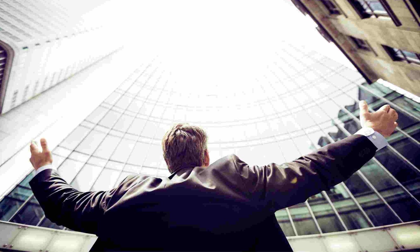 Confident businessperson with arms raised toward tall buildings, symbol of success